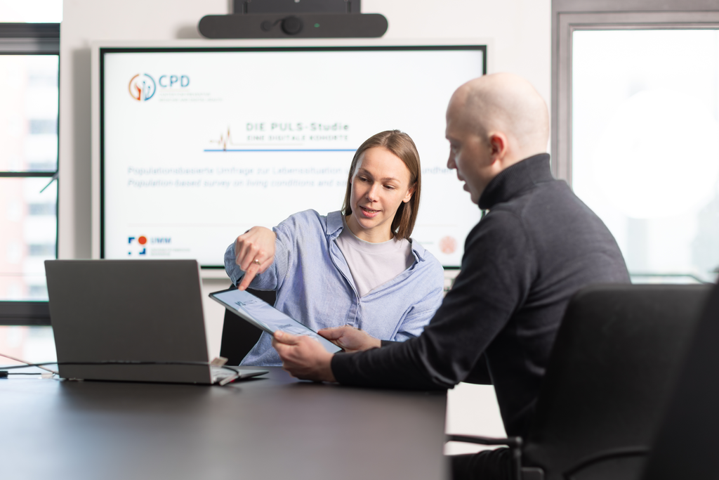 Wissenschaftlerin zeigt Nutzendem die von Data4Life erstellte Studienapp auf dem Smartphone